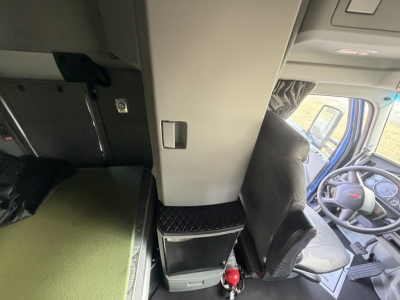 Cab interior of a 2020 Kenworth T680 showing driver seat, dashboard, and center console with green sleeper mattress and storage drawers.
