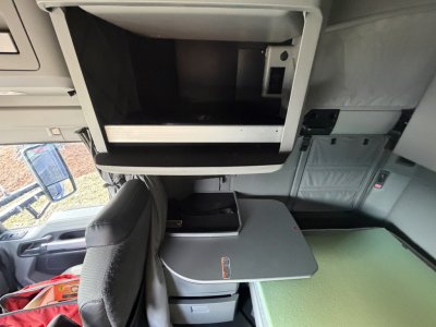 Cab interior of a Kenworth T680 with a fold-out sleeper table and open overhead compartment showing interior fittings.