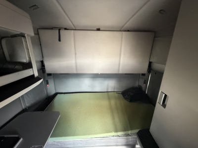Cab interior of a 2020 Kenworth T680 sleeper truck showing a cargo area with a green floor, side cabinets, and a rear bulkhead.