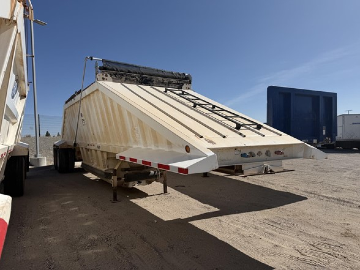 Dump trailer with air ride suspension in a yard showing steel bottom dump and open tailgate.