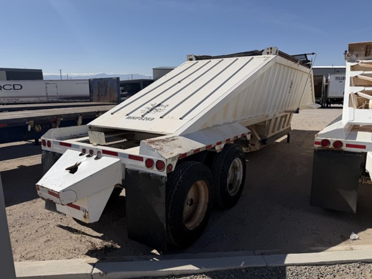 Dump trailer with air ride, steel bottom, rear view showing hydraulic tailgate and dual rear axles; white with reflective tape.