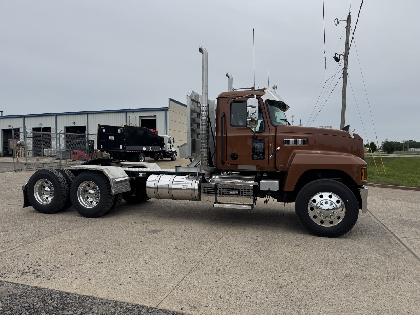 Truck cab and chassis of a new 2027 Mack PI64T conventional daycab showing aluminum fuel tanks and exhaust stacks.