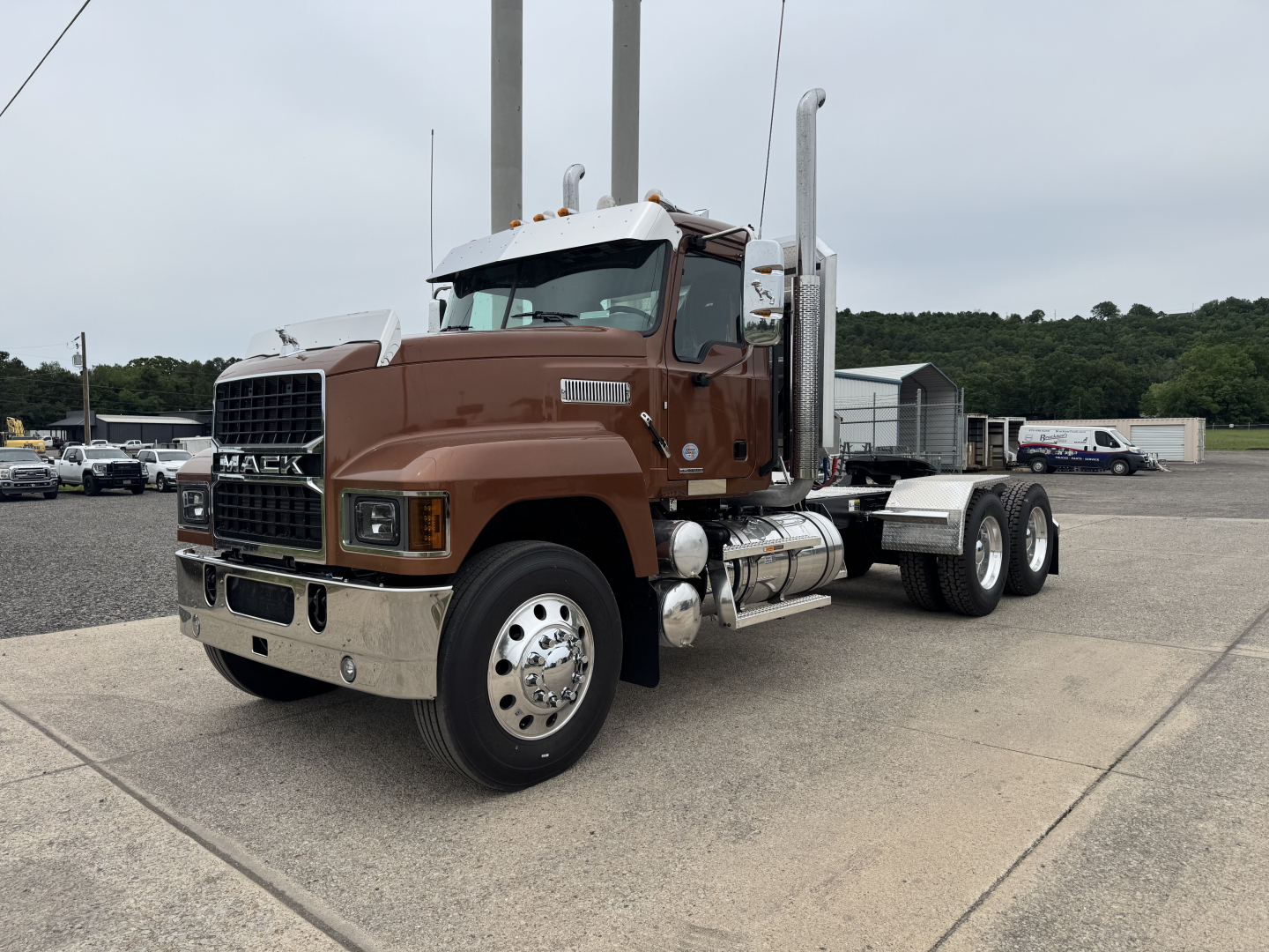 Brown 2027 Mack PI64T conventional daycab truck side view with dual exhaust stacks and chrome bumper.