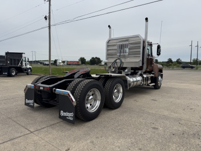 Mack PI64T tractor-trailer chassis showing rear triple axle with black mudflaps and fuel tanks, chrome exhaust stacks, and silver sleeper cab in background.