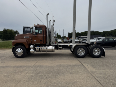 2007 Mack PI64T? Wait the listing says 2027 Mack PI64T but image shows a brown cabover-style? The visible text on components includes no legible labels clearly; a truck with dual rear axles, metal fuel tanks, exhaust stacks, chrome wheels.
