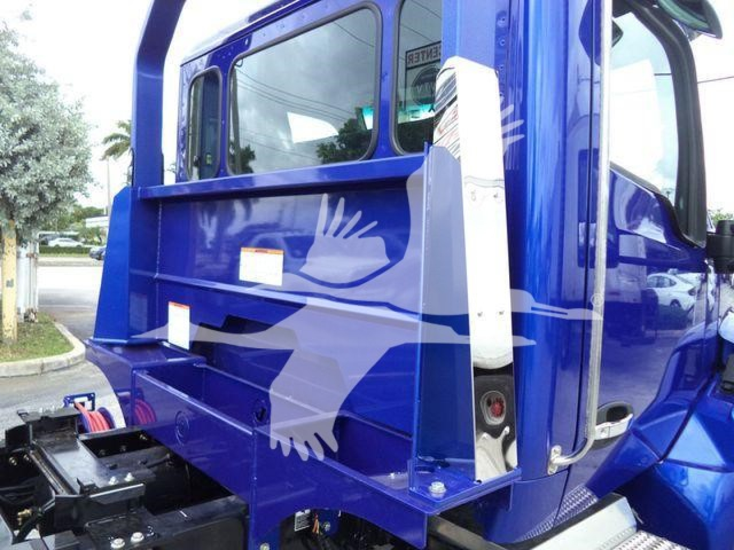 Truck cab back view of blue 2025 Kenworth T280 with rollback equipment and partial side mirror in foreground.