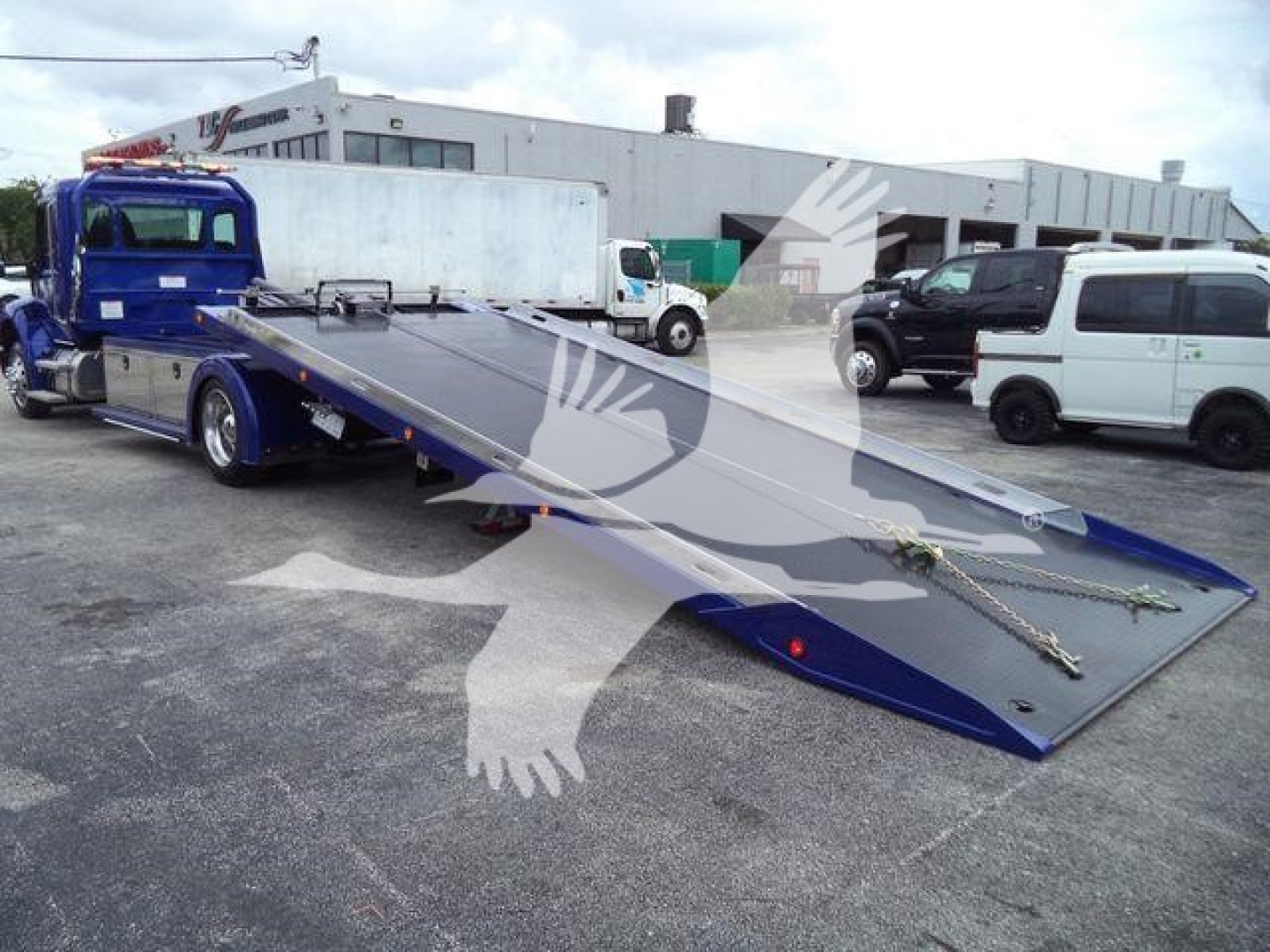 Kenworth T280 rollback truck with a long lowered flatbed; visible text includes KW2STEPSID stock number on the side of the cab area? The image shows a blue tow truck with an extended hydraulic flatbed in a yard.