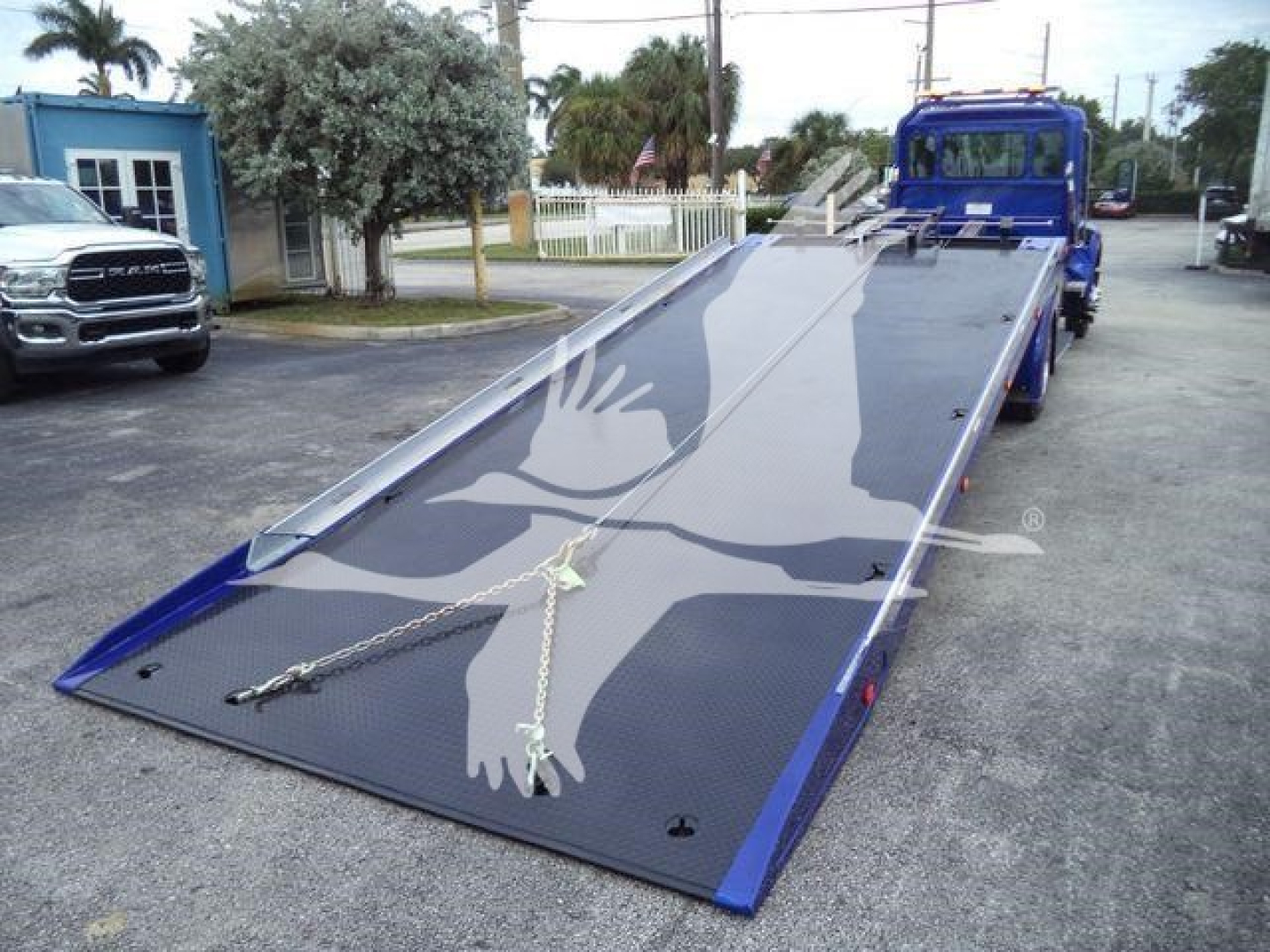 Kenworth truck flatbed tow truck with hydraulic wheel lift in blue, ramp extended and visible chains.
