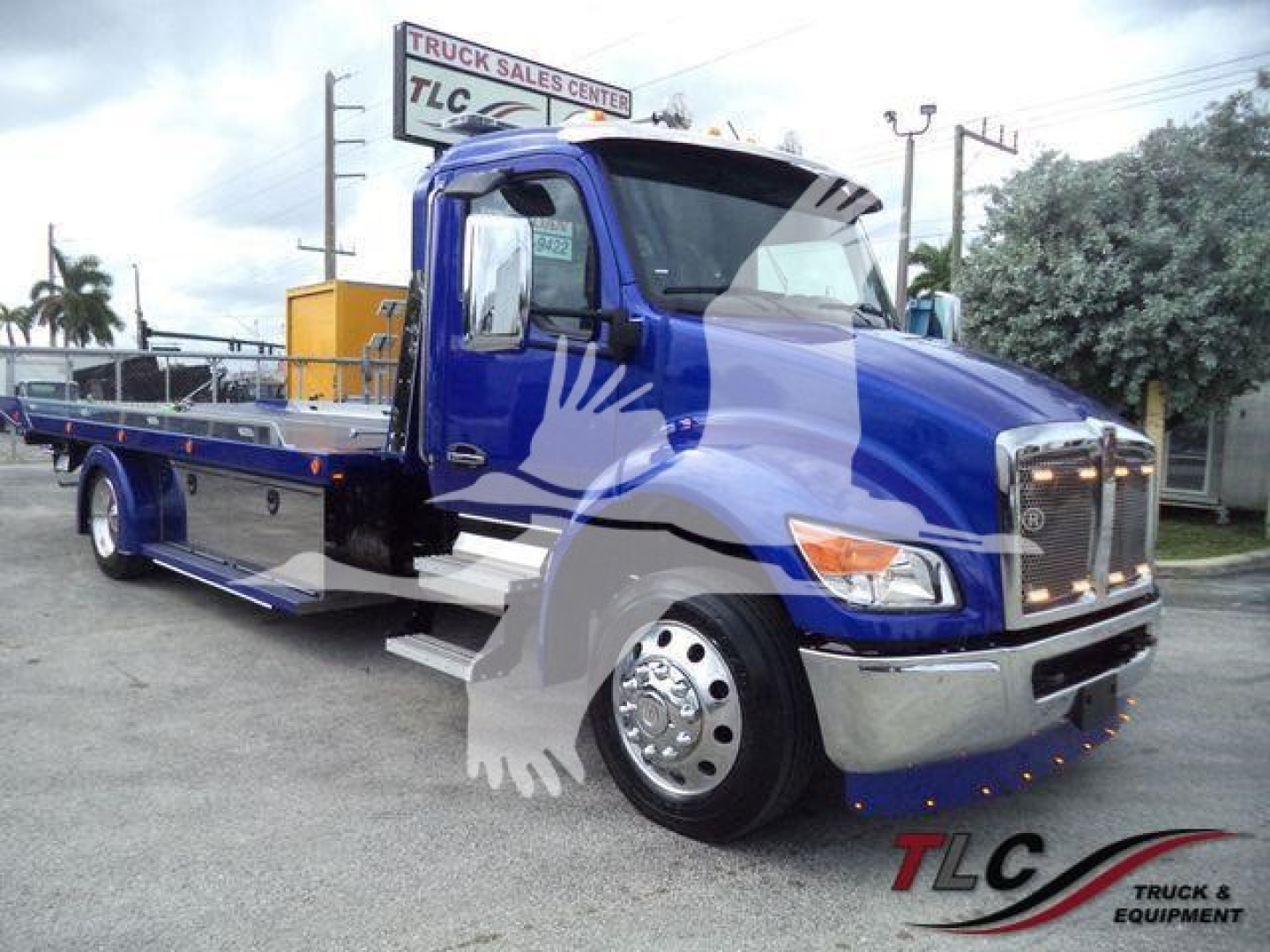 Kenworth T280 rollback truck in blue with chrome bumper and flatbed, showroom lot in background. TLC Truck & Equipment logo watermark.