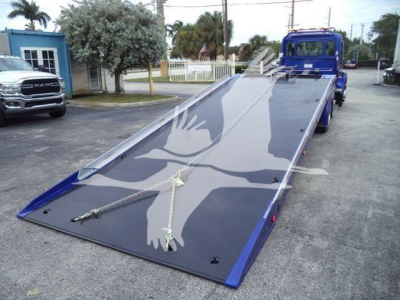 Kenworth truck flatbed tow truck with hydraulic wheel lift in blue, ramp extended and visible chains.