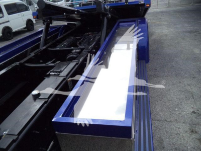 Kenworth T280 rollback truck chassis exposed with hydraulic lines and metal framework, blue bodywork, white reflective panels, bed area visible.