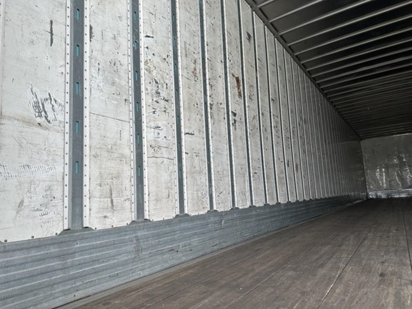Trailer interior showing wooden floor and metal side walls with vertical rails; empty cargo space.