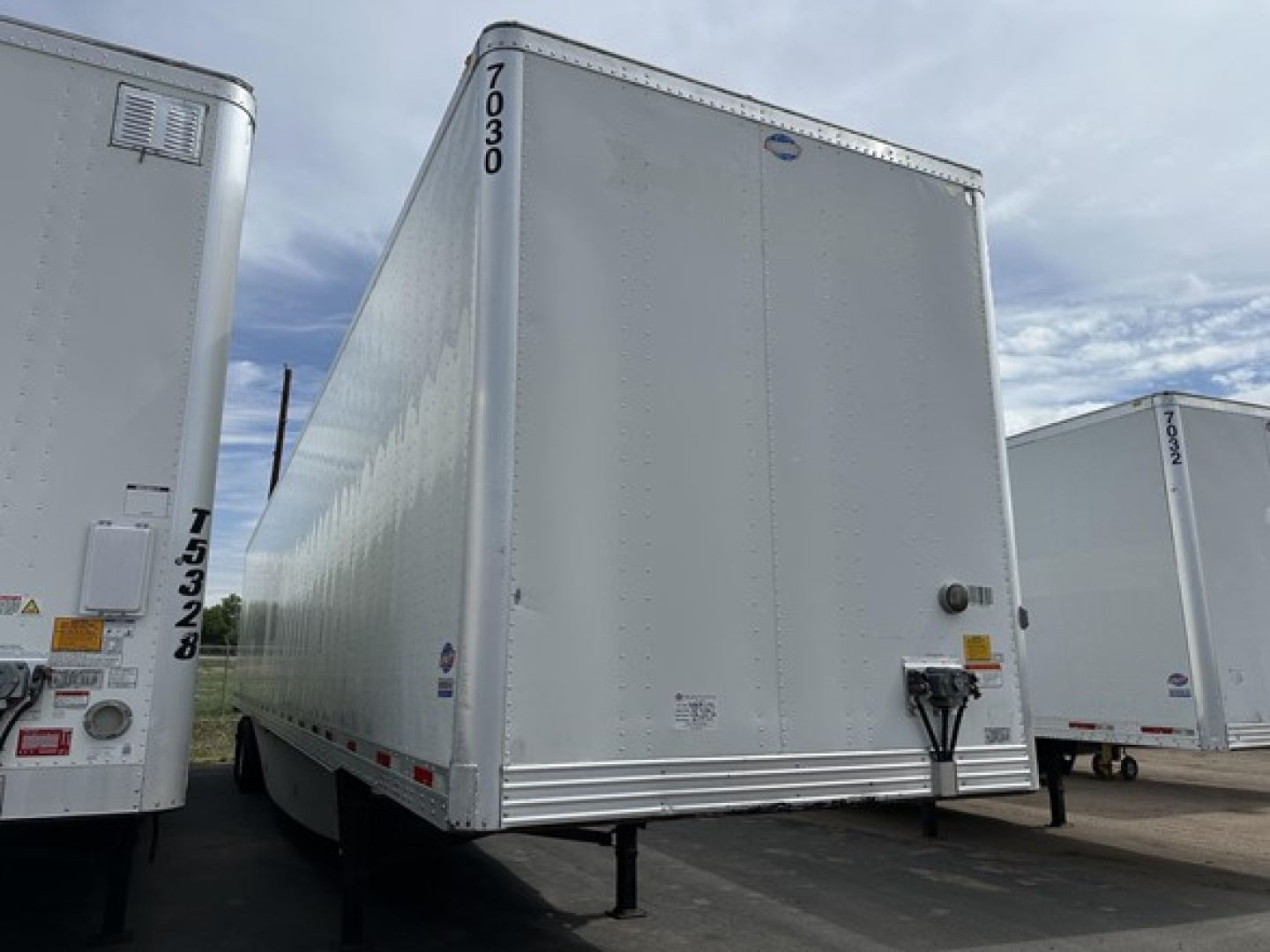 Trailer side view showing 2016 Utility 4000Dx box trailer with raised front and rear corner posts, black hitch, and numbers 17030 on top corner; other trailers visible.