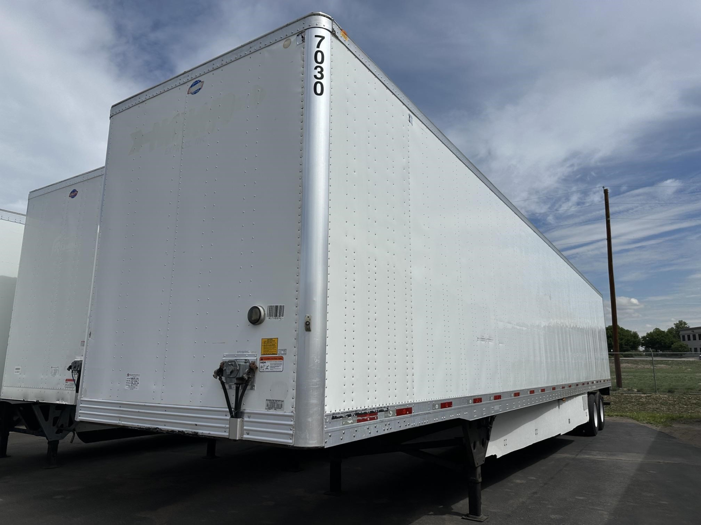 Trailer side view showing 2016 Utility 4000DX cargo trailer with registration tags and rear doors, tall vertical number 7030 on front corner, reflective tape along lower edge.