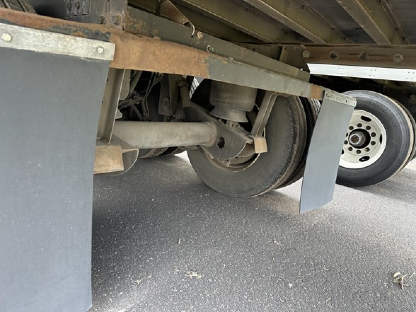Trailer undercarriage showing axle, suspension, and wheel assembly with mud flaps and steel frame.