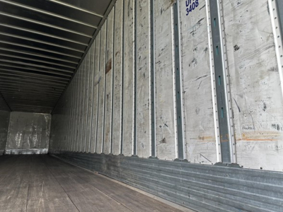 Trailer interior showing corrugated metal wall panels, wooden floor, and side rails in a utility trailer.