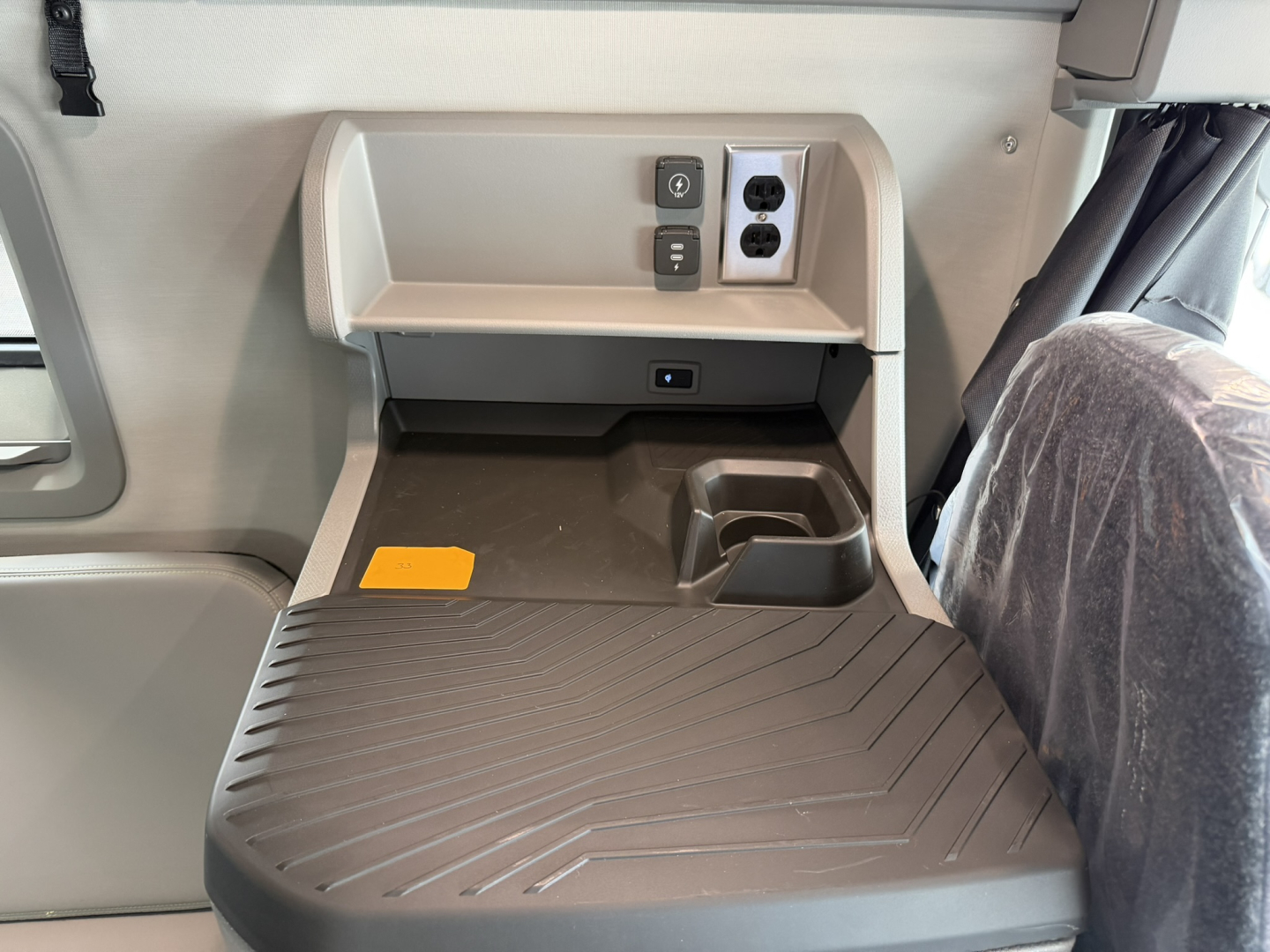 Tractor cab interior of a 2027 Volvo VNL64T860 showing a storage shelf, power outlets, and a textured rubber floor mat in the sleeper area.