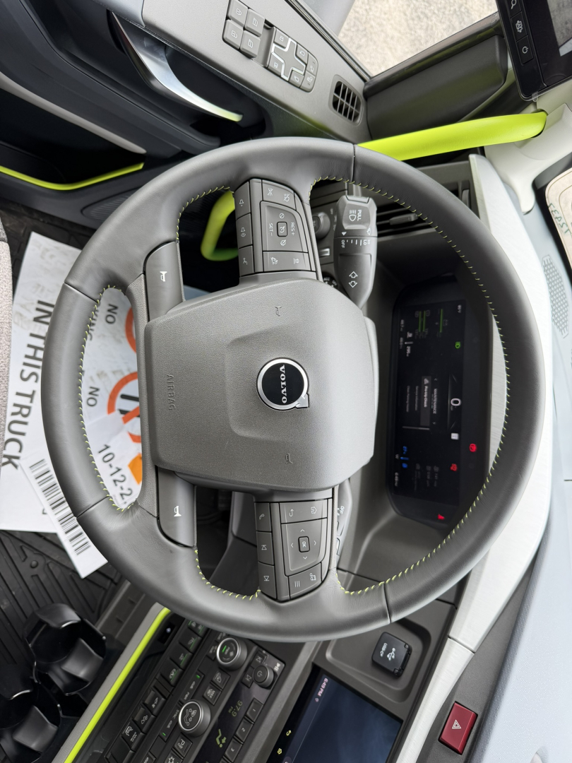 Volvo cockpit steering wheel with Volvo logo and control buttons in view. Dashboard display and center console visible.