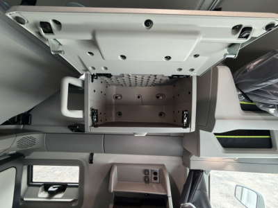 Truck cab interior showing overhead pass-through storage with open overhead compartment, light gray panels, and control switches. Volvo VNL sleeper cab layout.
