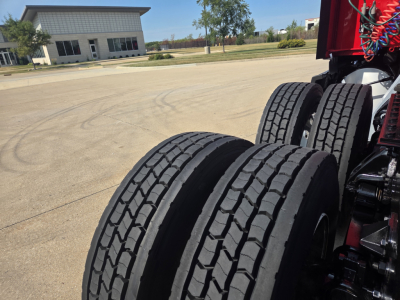 Kenworth T680 truck chassis showing dual rear axles with tires and suspension components in an outdoor lot.