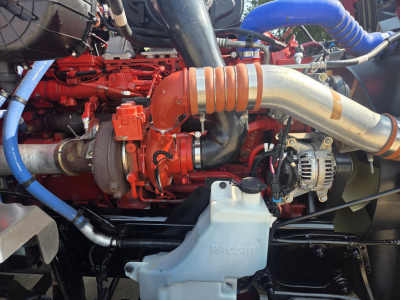 Kenworth T680 engine bay showing red engine block with large orange intake tube and silver exhaust pipes.