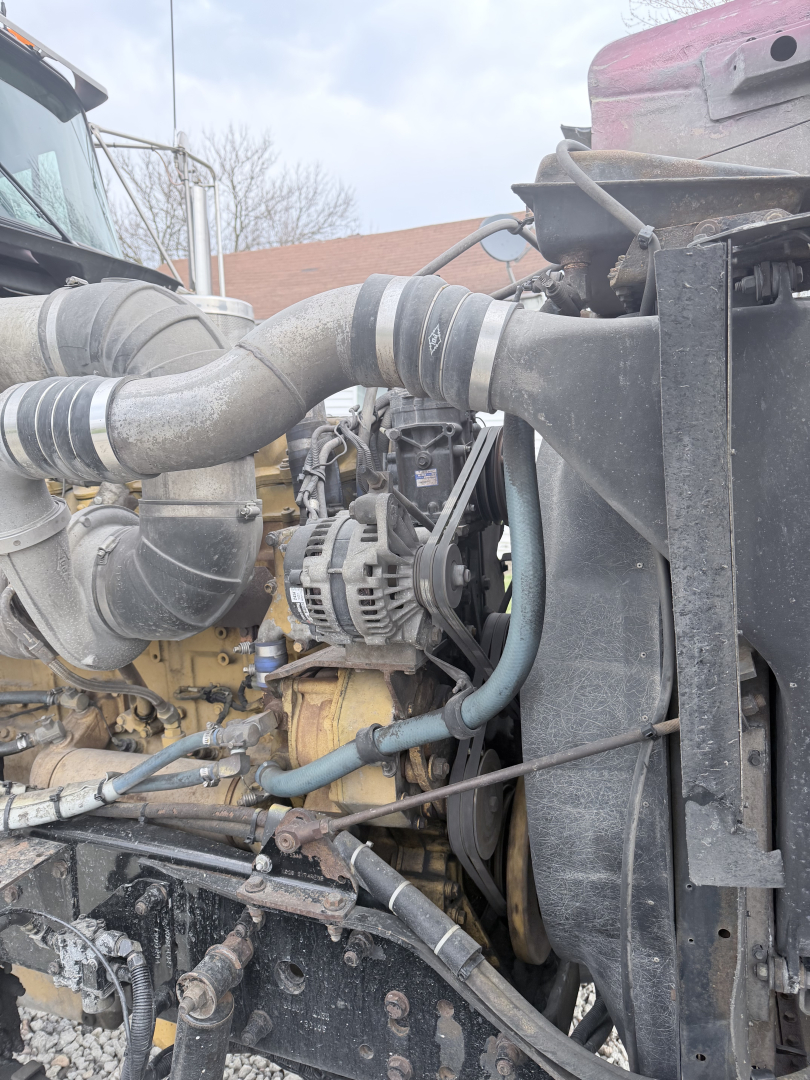 Kenworth W900L engine bay showing large turbo intake pipe, radiator, hoses, alternator, and engine components.