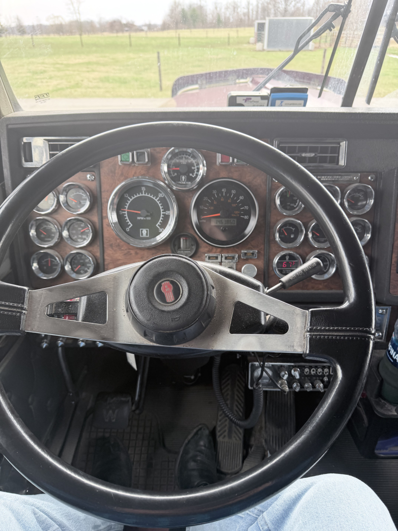 Steering wheel and gauge cluster in a Kenworth W900L interior showing multiple round gauges and a woodgrain dash