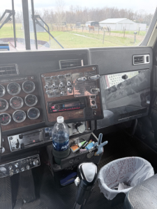 Kenworth W900L truck cabin dashboard view with metal control panel, gauges, and gear shifter visible.