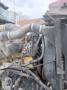 Kenworth W900L engine bay showing large turbo intake pipe, radiator, hoses, alternator, and engine components.