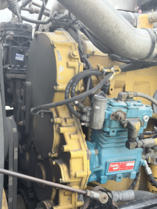 Kenworth W900L engine bay showing yellow engine block with cooling fan housing and blue fuel injection pump/valve cover, hoses and air intake plumbing visible.
