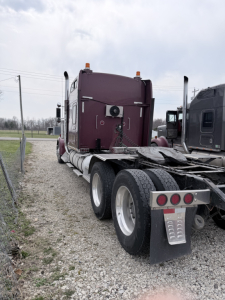Kenworth W900L tractor rear view showing dual rear axles, sleeper cab, purple maroon paint, chrome fuel tanks, and rear mud flaps.