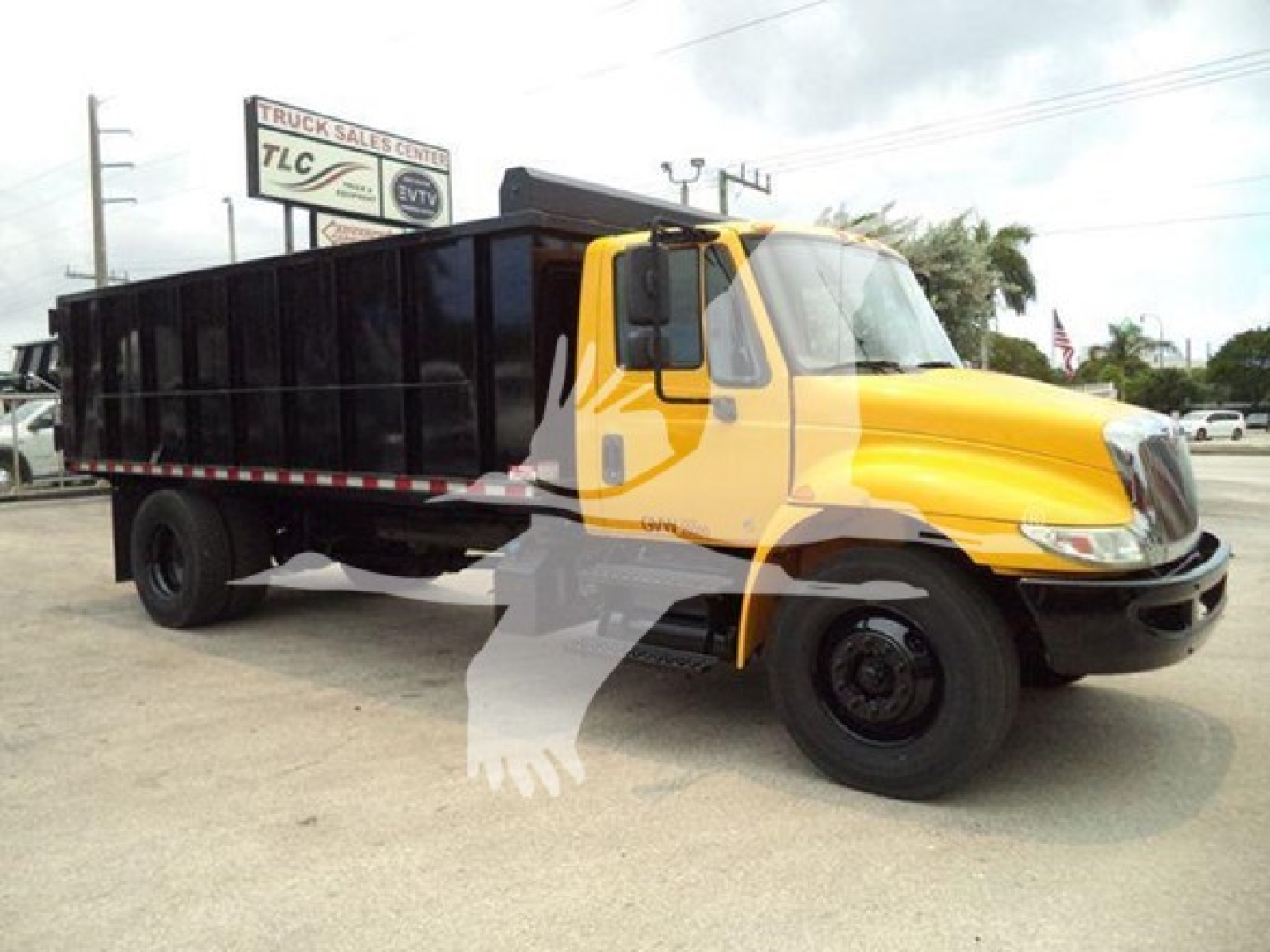 School bus-style yellow front cab with black dump bed truck, driving on lot under overcast sky; side view shows long black cargo bed.