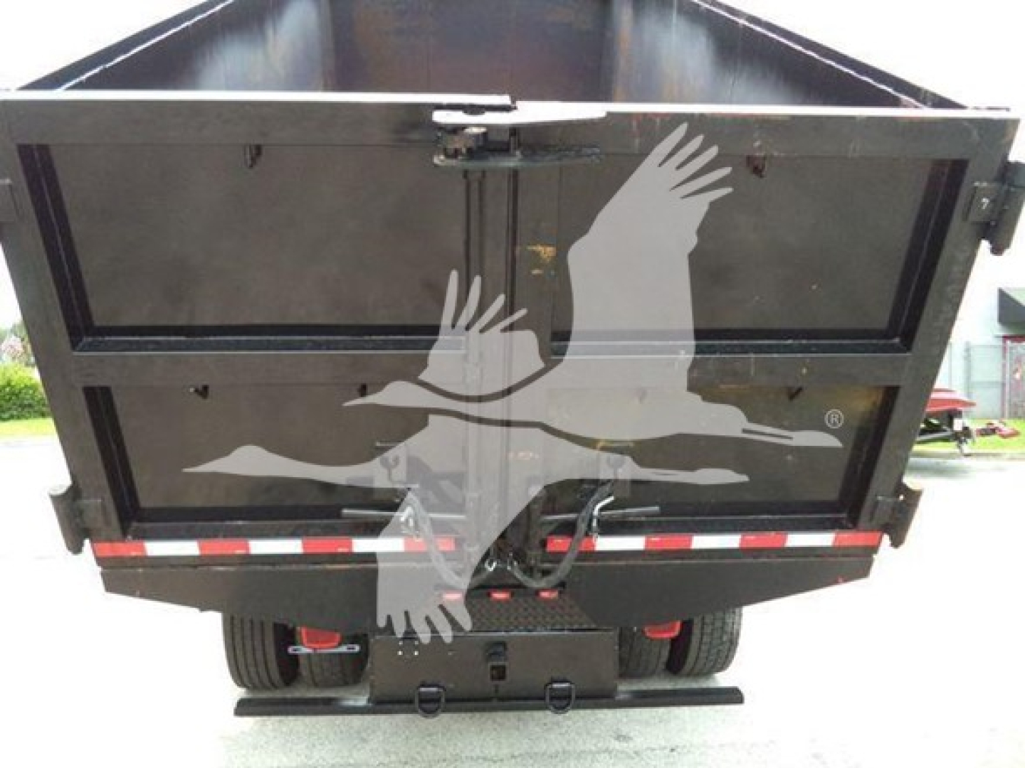 Dump truck tailgate view showing dump bed and rear underride with dual tires, rear bumper, and taillights.