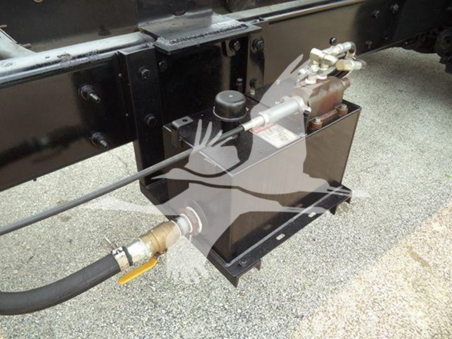 [Component] Hydraulic power unit with reservoir and hoses mounted under the dump truck frame showing fittings and control valves.