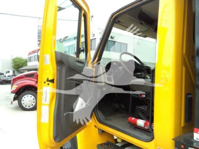 Truck cab interior with yellow exterior. Open door shows grey interior panel and steering wheel; label stickers visible on door frame; fire extinguisher on floor area; outside another red truck visible.