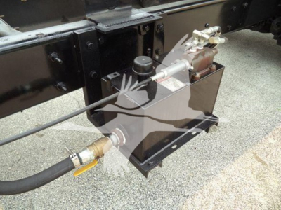 [Component] Hydraulic power unit with reservoir and hoses mounted under the dump truck frame showing fittings and control valves.