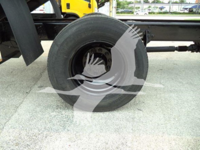 Truck wheel and suspension component visible under a dump truck, highway surface beneath, with partial view of chassis and axle.
