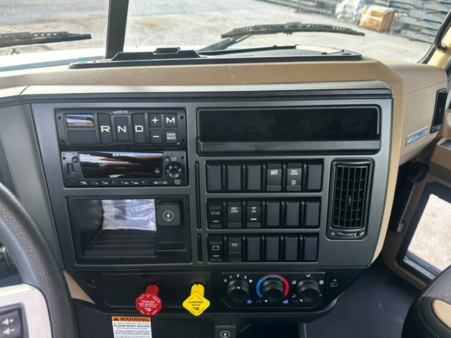 Mack GR64F cab dash view showing steering area and control panel with R N D + M gear positions, climate controls, and switches.