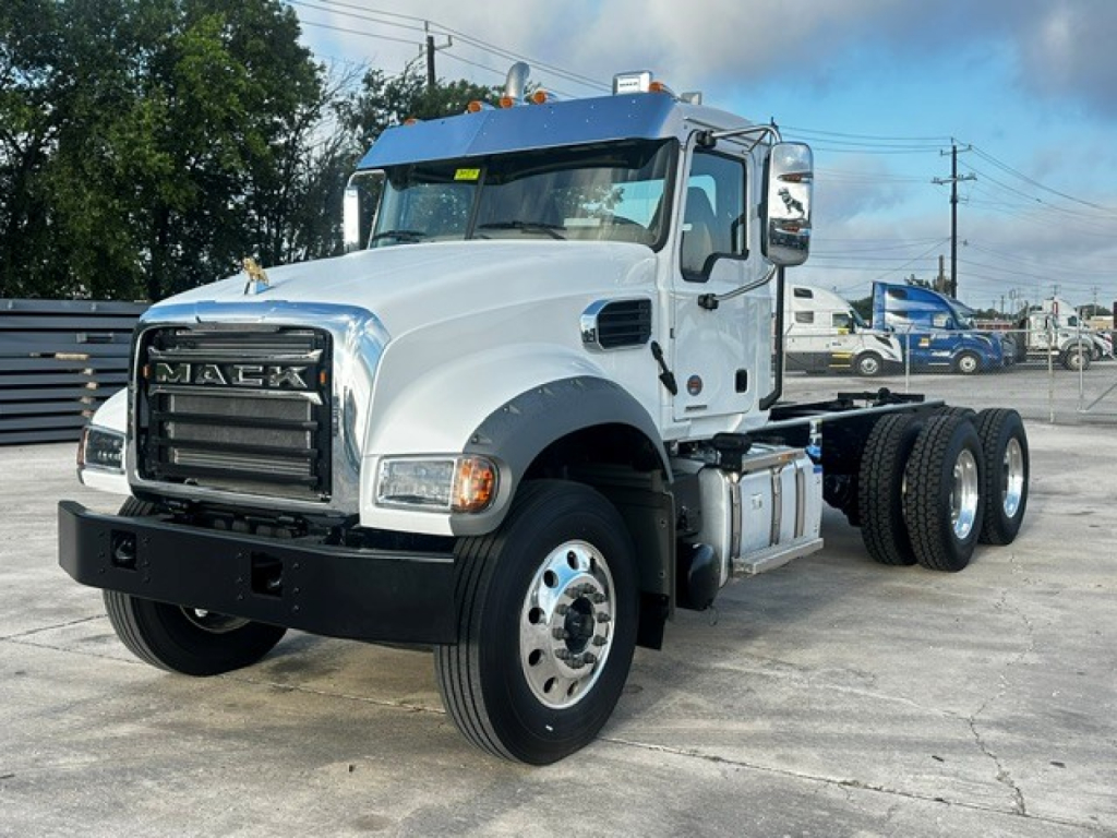 Mack GR64F dump truck front-left view showing chrome grille, white cab, large bumper, and dual rear axles.