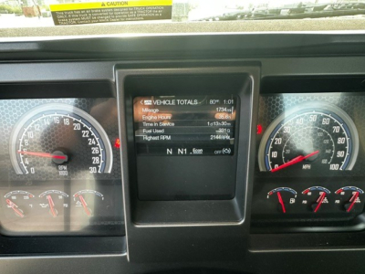Dashboard view of a 2027 Mack GR64F showing instrument cluster and central display with vehicle totals: mileage 1734.1, engine hours 65.0, time in service 1:01, fuel used 0, highest RPM 0, gear indicator N NN.