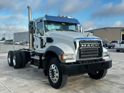 Mack GR64F dump truck in a parking lot showing front grille with MACK lettering, chrome bumper, dual exhaust stacks, and large side mirrors.