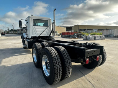 Truck chassis with dual rear axles, cab in front, Mack GR64F configuration. View from rear-left showing frame, dual rear tires, exhaust stack, and fifth-wheel area.