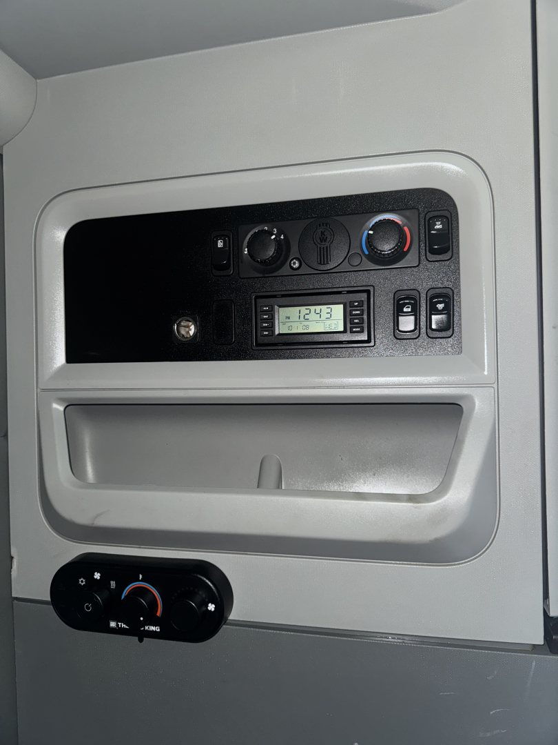 Dashboard panel of a 2015 Kenworth T680 sleeper cab showing HVAC controls and a small digital radio/display.