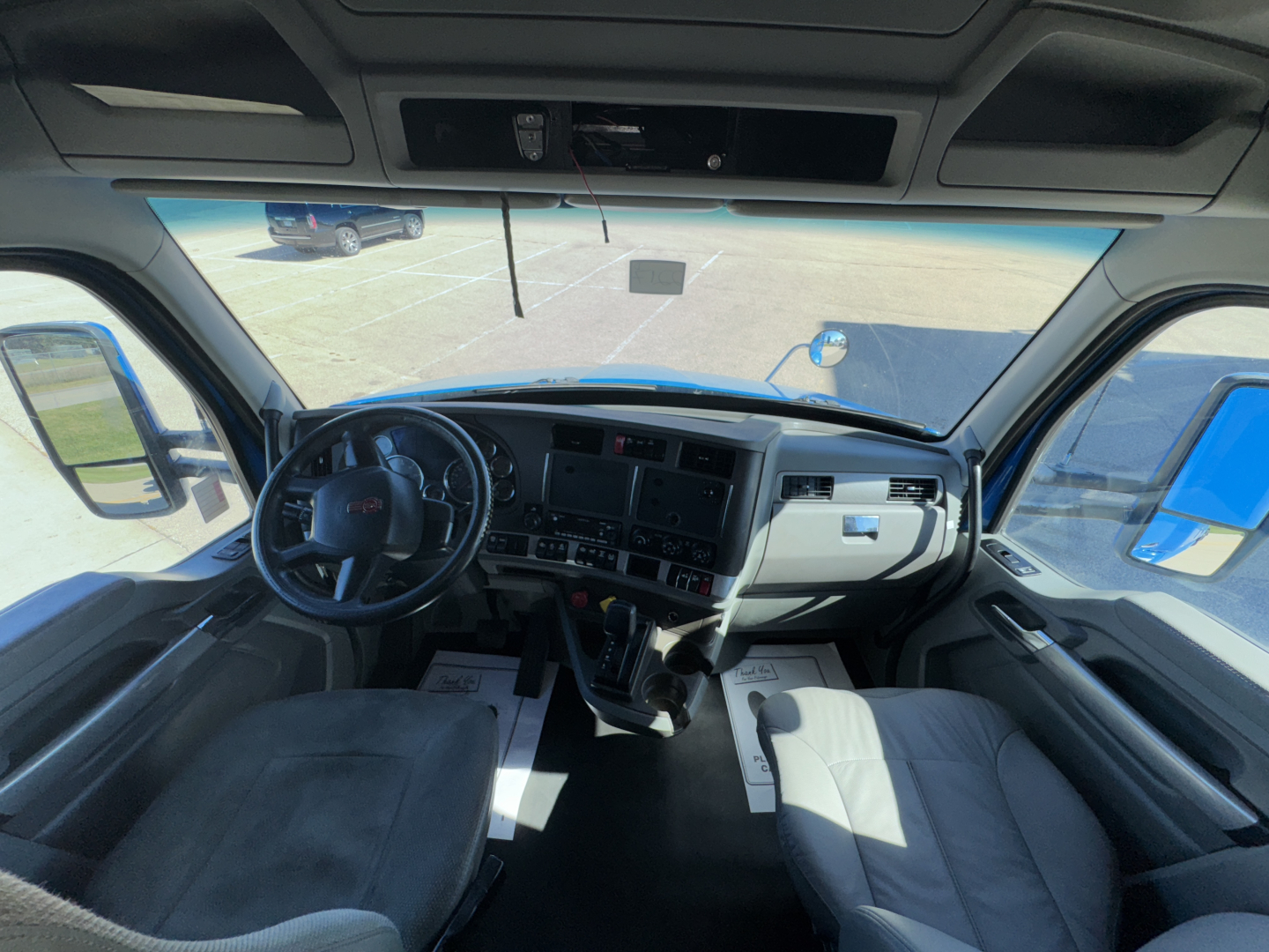 Truck cab interior of a 2015 Kenworth T680 showing steering wheel, dashboard, and captain seats with gear shifter.