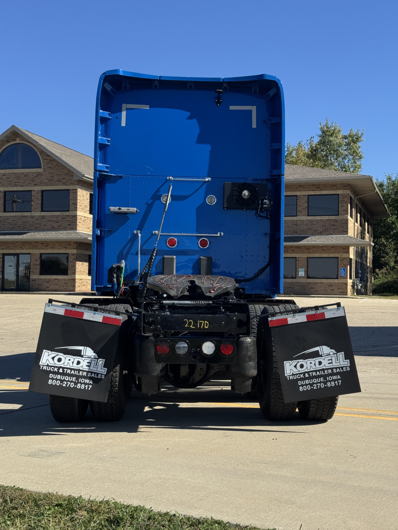 Kenworth T680 rear view showing blue cab interior and tail area with mudflaps and rear stickers.