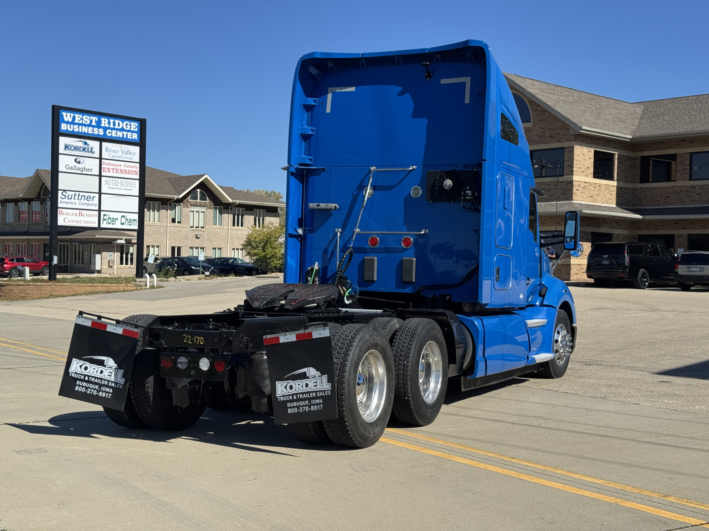 Truck tractor rear view showing fifth wheel, dual rear axles, blue cab, and black bumper with Kordel signs; no legible labels or fluid reservoirs visible.
