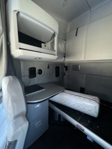 Kenworth T680 sleeper cab interior showing upper bunk, dashboard console, and seating area with storage drawers.