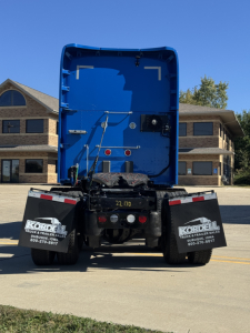 Kenworth T680 rear view showing blue cab interior and tail area with mudflaps and rear stickers.