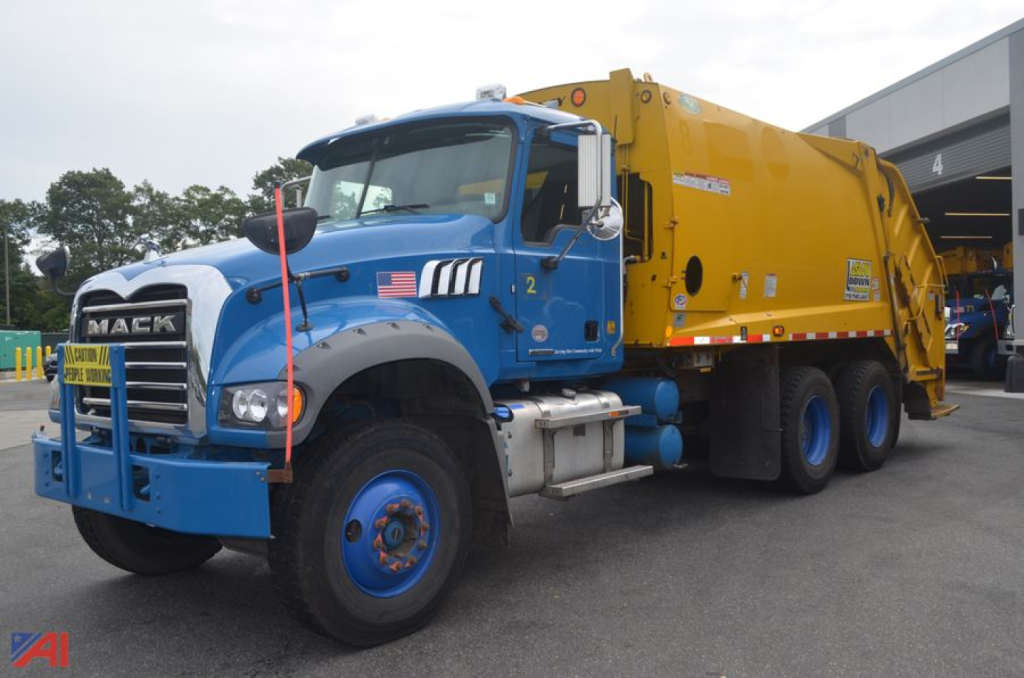 Mack Granite dump truck with blue cab and yellow body, front grill guard, large tires, and American flag decal on door.