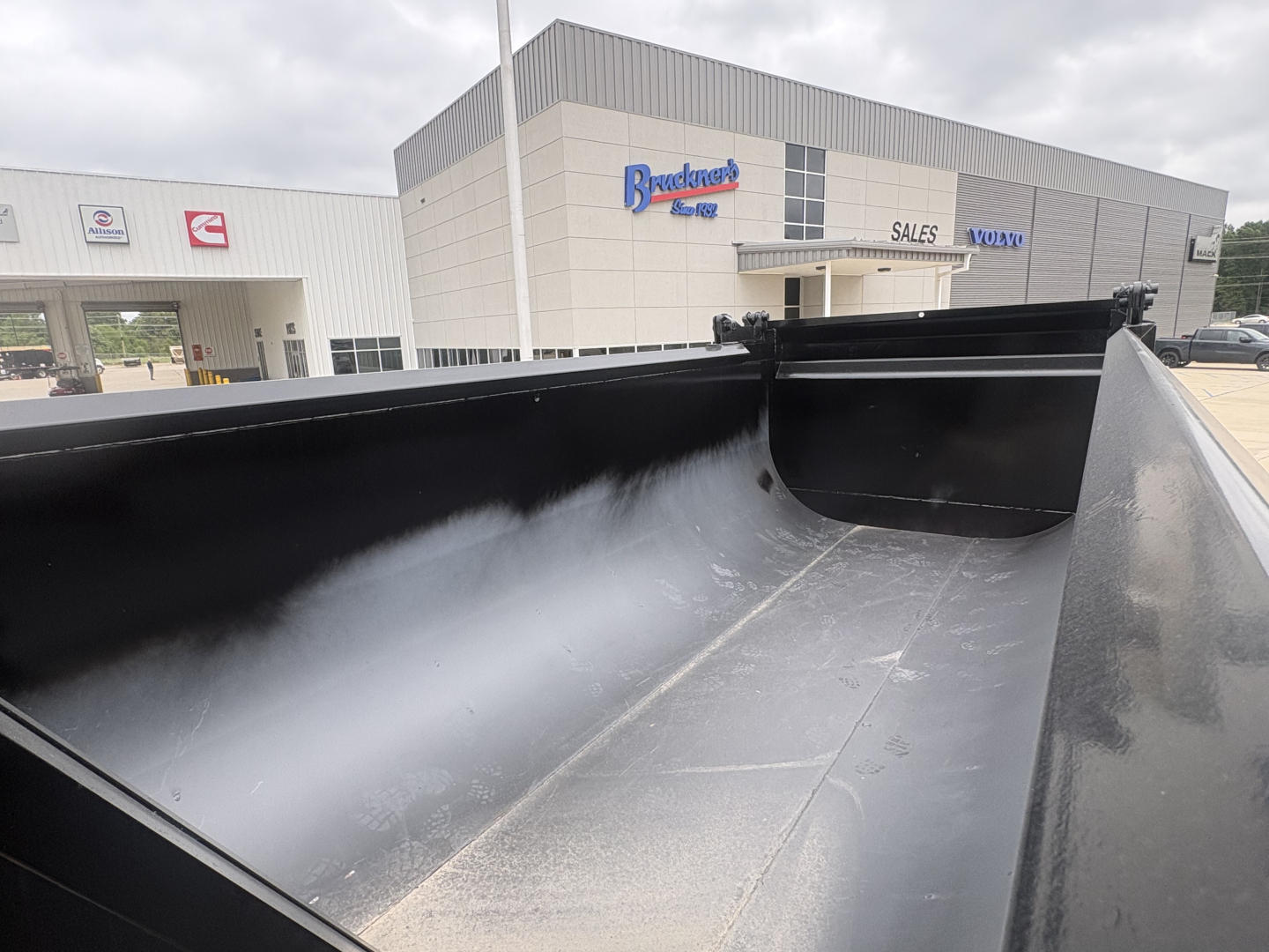 Dump truck bed interior with black metal sides and front riser, visible in a Mack GR84F listing near dealership building.